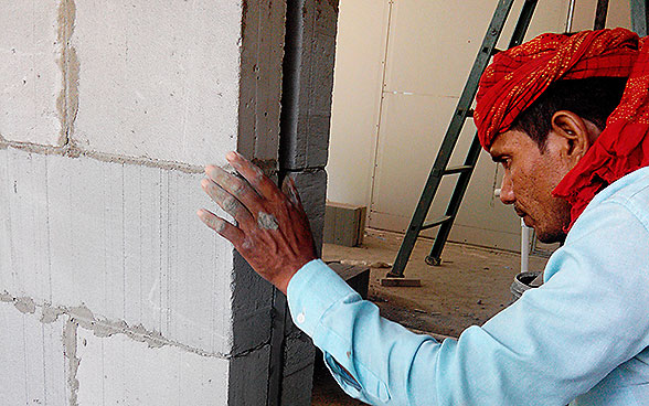 Un operaio indiano costruisce un muro con mattoni di cemento LC3.
