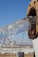 Wasser fliesst aus einem Leitungsrohr. Im Hintergrund sieht man das Flüchtlingslager Azraq