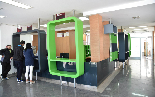 A woman and two men stand at the counter of a local administration and discuss their concerns with the official.