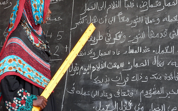 Una giovane donna tiene in mano un righello e legge cosa c’è scritto su una lavagna; in questo modo beneficia dei servizi offerti da un centro di alfabetizzazione a Oum Hadjer, città della regione di Batha in Ciad. © DSC