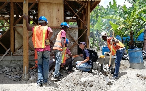 Eine Expertin des SKH vor einer Baustelle mit haitianischen Fachleuten. 