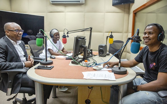 Sur l'image, on voit trois personnes dans un studio de radio en train d'enregistrer une émission.