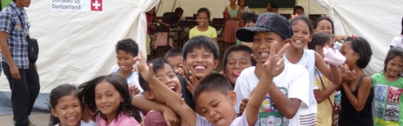 Filipino children are gathered in front of a tent provided by the Swiss Humanitarian Aid