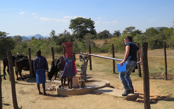 Un’esperta del CSA pompa acqua da un pozzo circondato da bambini africani.