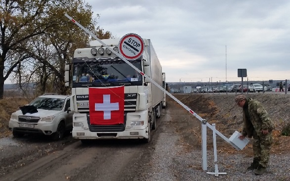 A soldier raises a barrier, opening the way for a Swiss Humanitarian Aid lorry.