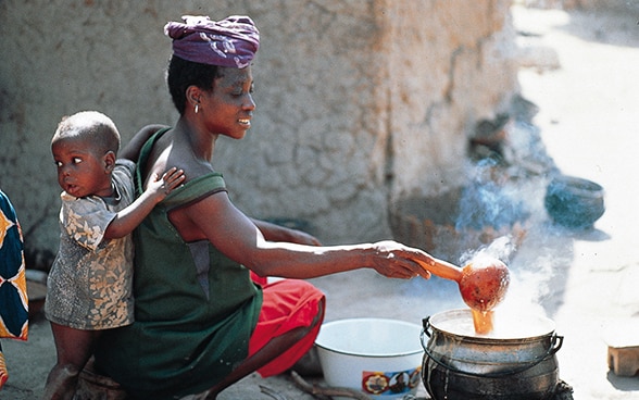 Femme préparant à manger sur le sol avec un enfant appuyé contre elle au Mali