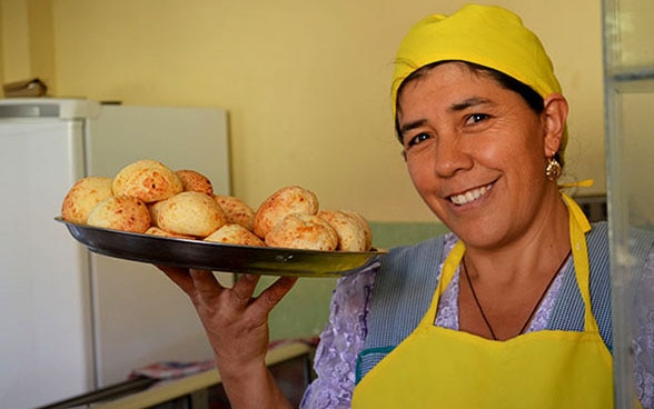 Doña Silvia in Arbeitskleidung mit einem Tablett Brötchen. 