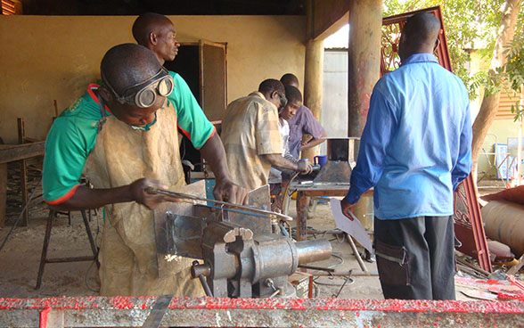 Angehende Schweisser arbeiten in einer Werkstatt unter der Aufsicht eines Lehrmeisters