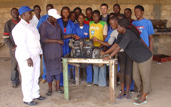 Frauen und Männer in Burkina Faso stehen vor und neben einem Tisch, auf dem sich eine Maschine befindet.