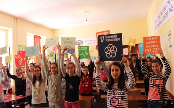 Dans la salle de classe, des enfants tiennent une pancarte où sont inscrits les objectifs de développement durable de l’Agenda 2030.