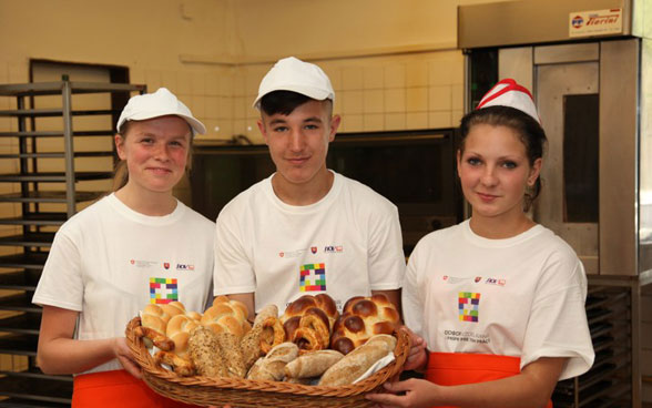 Tre giovani apprendisti panettieri mostrano il pane che hanno appena sfornato.