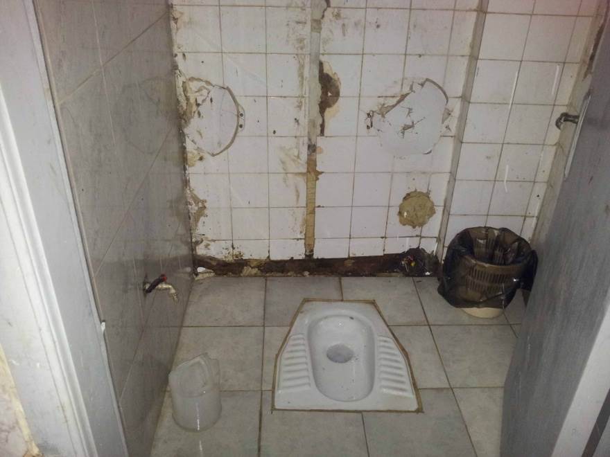 Des toilettes avec des murs aux carrelages endommagés.