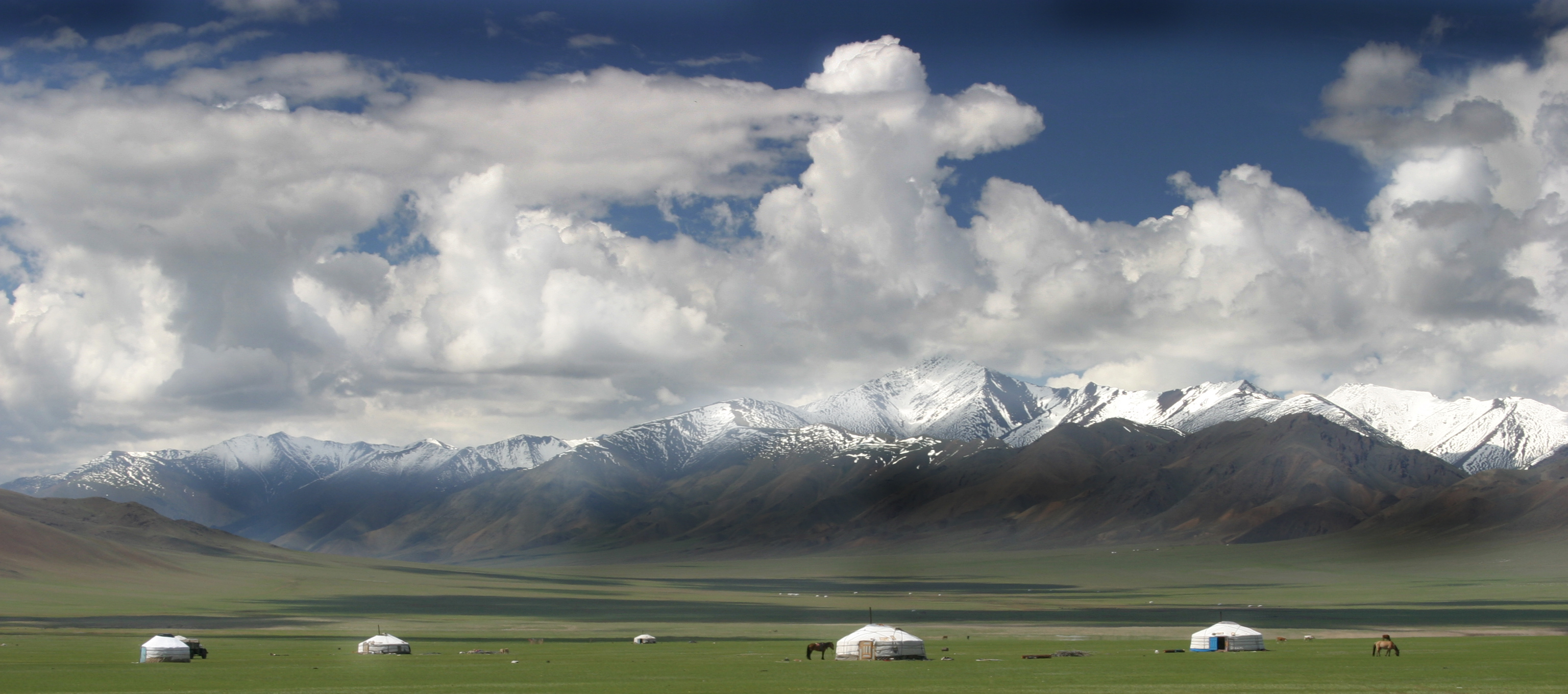 Cabañas diseminadas en una verde pradera, con el trasfondo de una cordillera nevada.