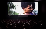 Sala buia di un cinema: sullo schermo due uomini si abbracciano