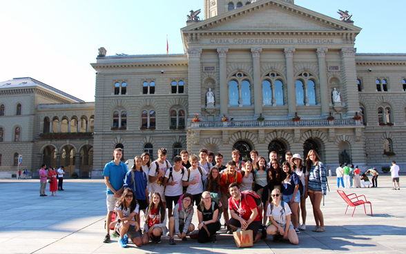 L'image montre un groupe de personnes devant le Palais fédéral. 