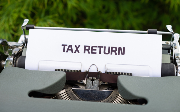 The words TAX RETURN in upper case written on a piece of paper sticking out of a typewriter.