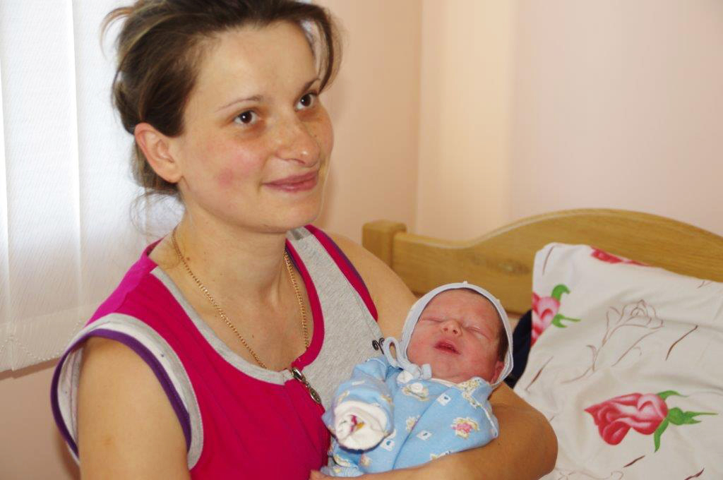 A smiling mother cradling her newborn baby in her arms.