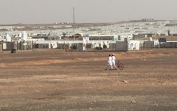 Two men, one of whom is pushing a bike, walk towards the Azraq refugee camp.