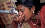 Frau trinkt Wasser von einem Wasserhahn.