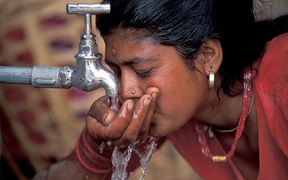 Woman drinks water from a tap. 
