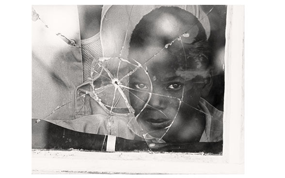 Un bambino mozambicano guarda attraverso un vetro perforato da un proiettile