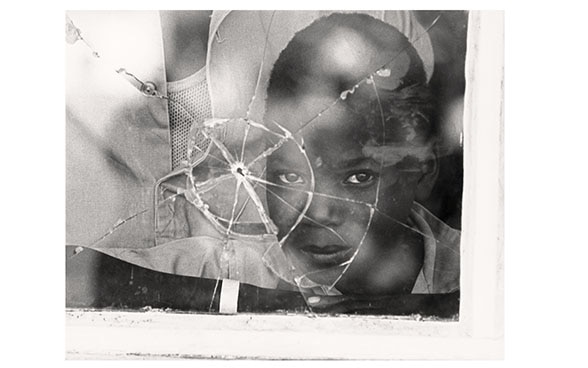 A Mozambican boy looks through a window with a bullet hole