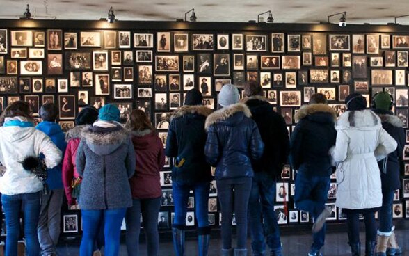 Un groupe de jeunes suisses regardent un mur où sont accrochés les portraits de victimes de l’Holocauste.