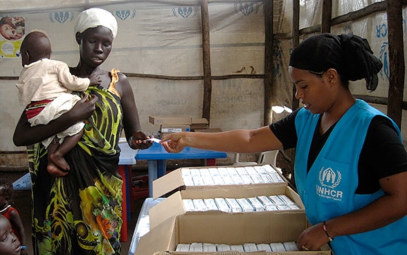 Une femme avec un enfant reçoit un bon d'alimentation dans une tente des Nations Unies.