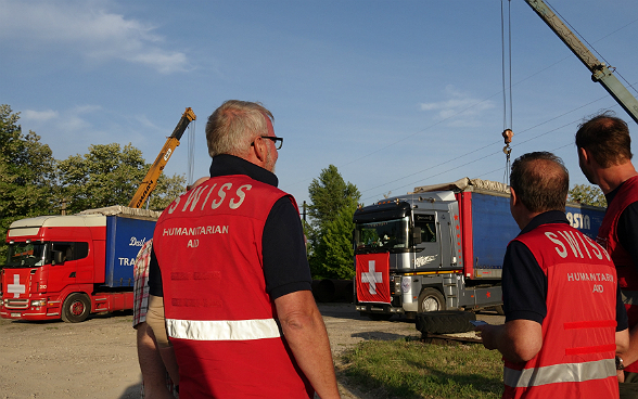 Trois membres de l’aide humanitaire suisse observent le chargement du matériel dans les camions. 