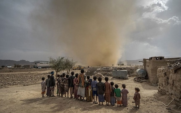 A group of African children watch a sandstorm in an arid sandy environment. 