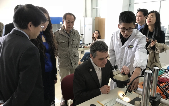 Le conseiller fédéral Ignazio Cassis est assis devant un microscope et entouré d’étudiants scientifiques de l’Académie chinoise des sciences