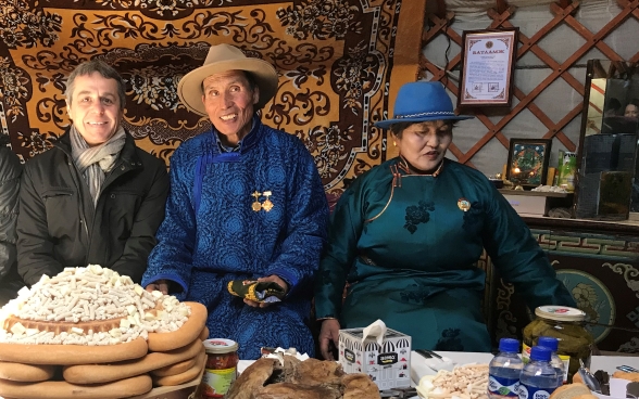 Federal Councillor Cassis sits at a richly laid table with two Mongolian cattle breeders.