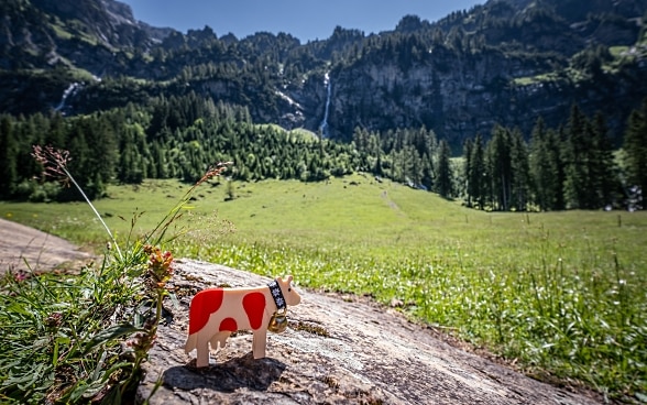Una mucca rossa punteggiata di legno si trova in un paesaggio montano svizzero.