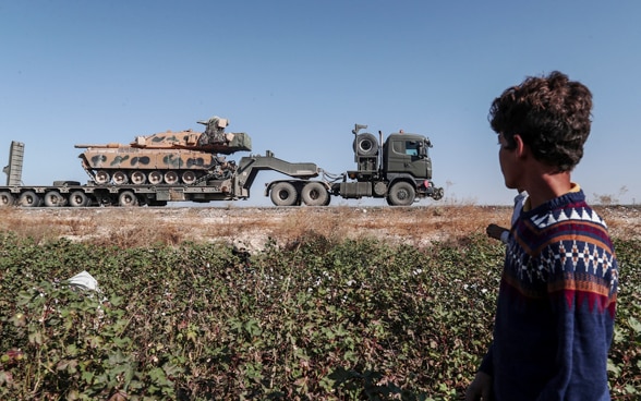 A worker in a cotton field in Sanliurfa region observes the passage of a Turkish military vehicle heading towards north-eastern Syria