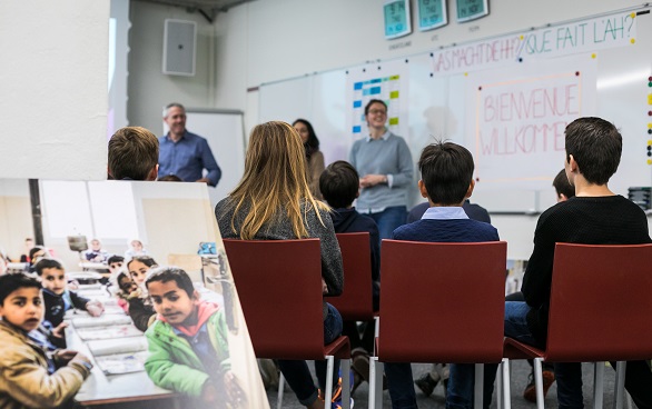 Kinder hören einer Frau zu, welche die Arbeit der Humanitären Hilfe der Schweiz präsentiert.