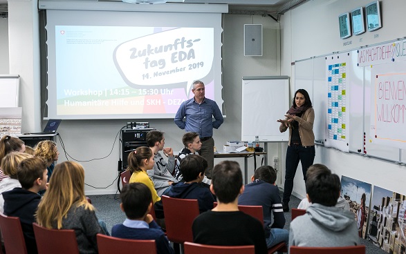 I bambini ascoltano una donna che presenta il lavoro dell'Aiuto umanitario della Svizzera.