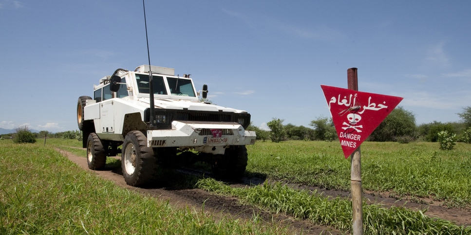 A mine-clearing vehicle drives into a field with a sign warning of the presence of mines.