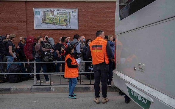 Les touristes font la queue pour monter dans un bus. Deux membres de l'ambassade d'Allemagne à Katmandou se tiennent à côté.