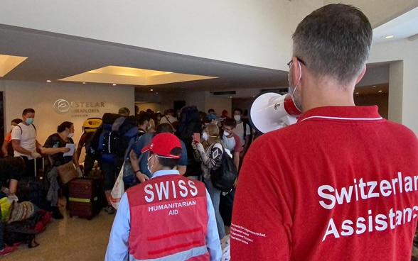 Ein Mitarbeiter der Schweizer Botschaft gibt mit einem Megafon Anweisungen für die Reisenden. 