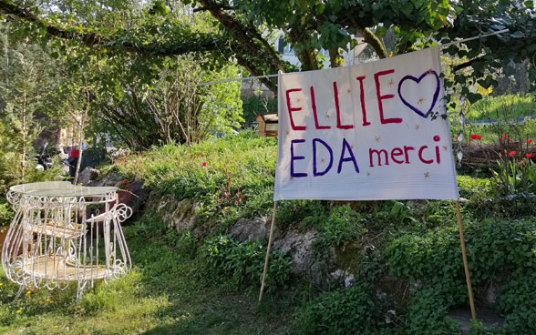 Ein Plakat steht in einem Garten, auf welchem «Ellie, EDA merci» steht. 