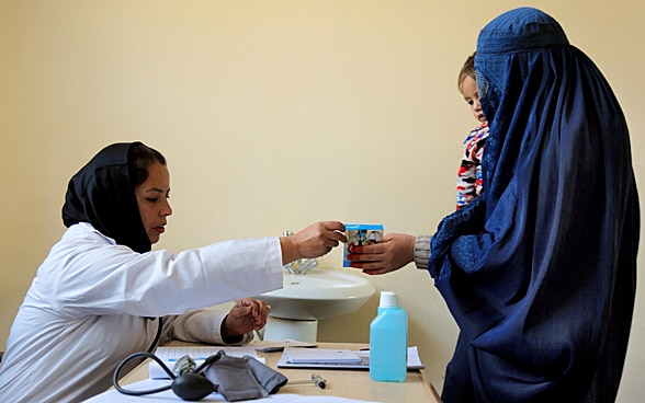 Eine Mutter mit ihrem Kind auf dem Arm erhält von einer Mitarbeiterin eines Spitals in Kabul/Afghanistan ein Medikament. 