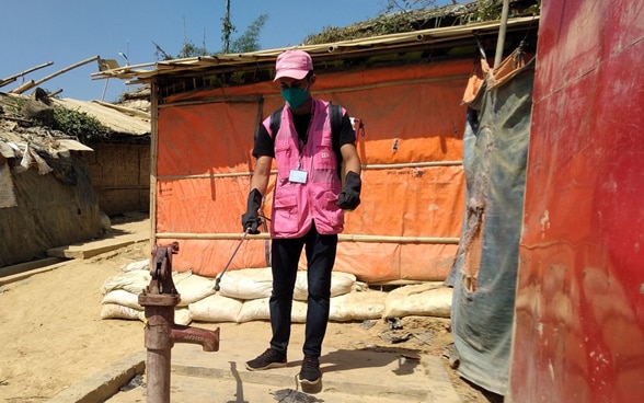 A man in a pink jacket disinfects a well in a refugee camp in Bangladesh. 