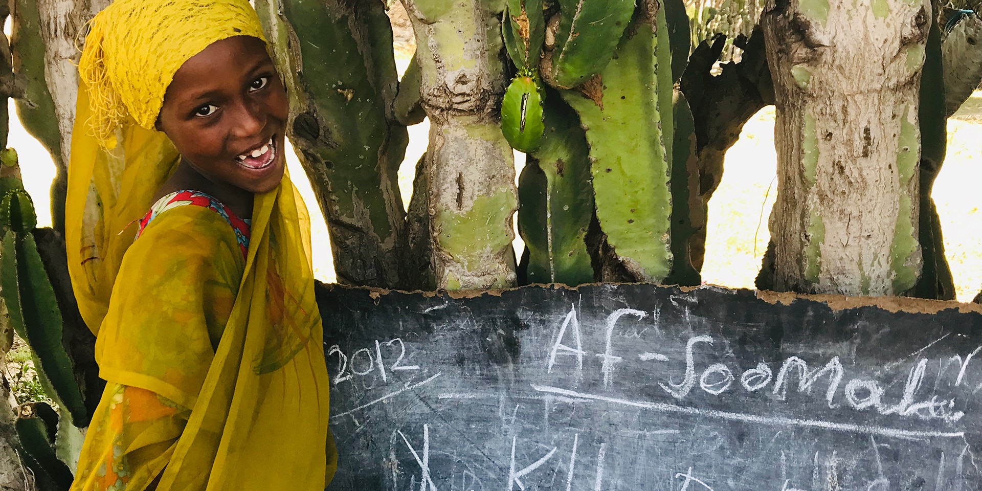  Une fille se tient devant un tableau noir en plein air et regarde dans la caméra (photo prise en Ethiopie) 