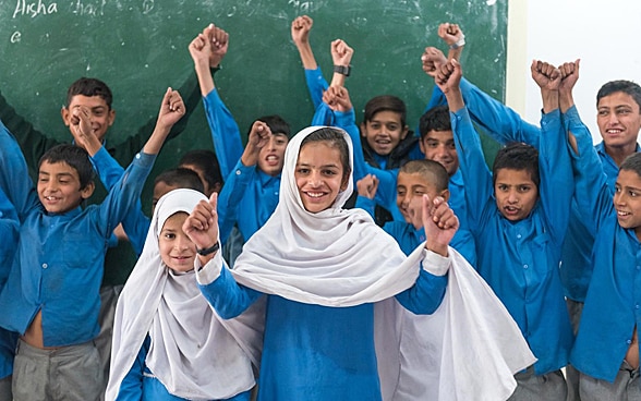  A school class in Pakistan stands in front of a blackboard and has fun.
