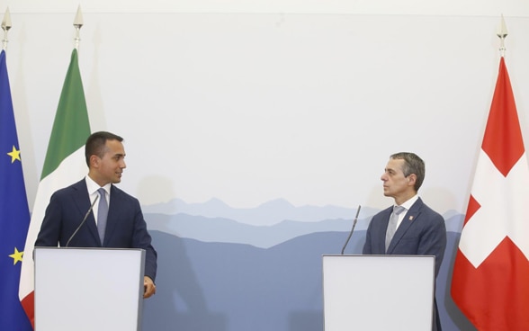 Le conseiller fédéral Cassis et le ministre italien des affaires étrangères Luigi Di Maio se tiennent chacun derrière un pupitre. Les drapeaux de la Suisse, de l'Italie et de l'UE sont visibles en arrière-plan.