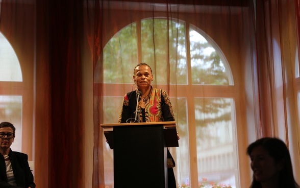 Patricia Danzi, Head of the Swiss Agency for Development and Cooperation stands at a lectern and speaks to diplomatic representatives in the hall.