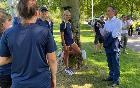 Federal Councillor Ignazio Cassis talks to track and field athletes outdoors. 