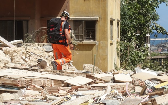 Un collaboratore dell’Aiuto umanitario della Confederazione cammina tre le macerie di una casa.