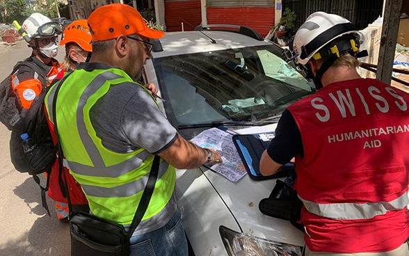 Quatre personnes sont debout près d'une voiture et discutent d’une carte de la région.