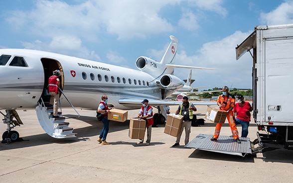 View of several experts from the Swiss Humanitarian Aid Unit form a human chain to transfer material from an aircraft to a truck.